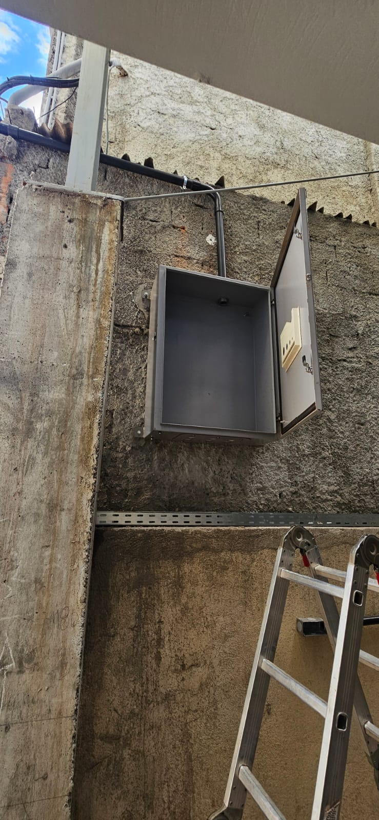 Instalação de caixa de painel elétrico externo em parede alta, com escada de apoio